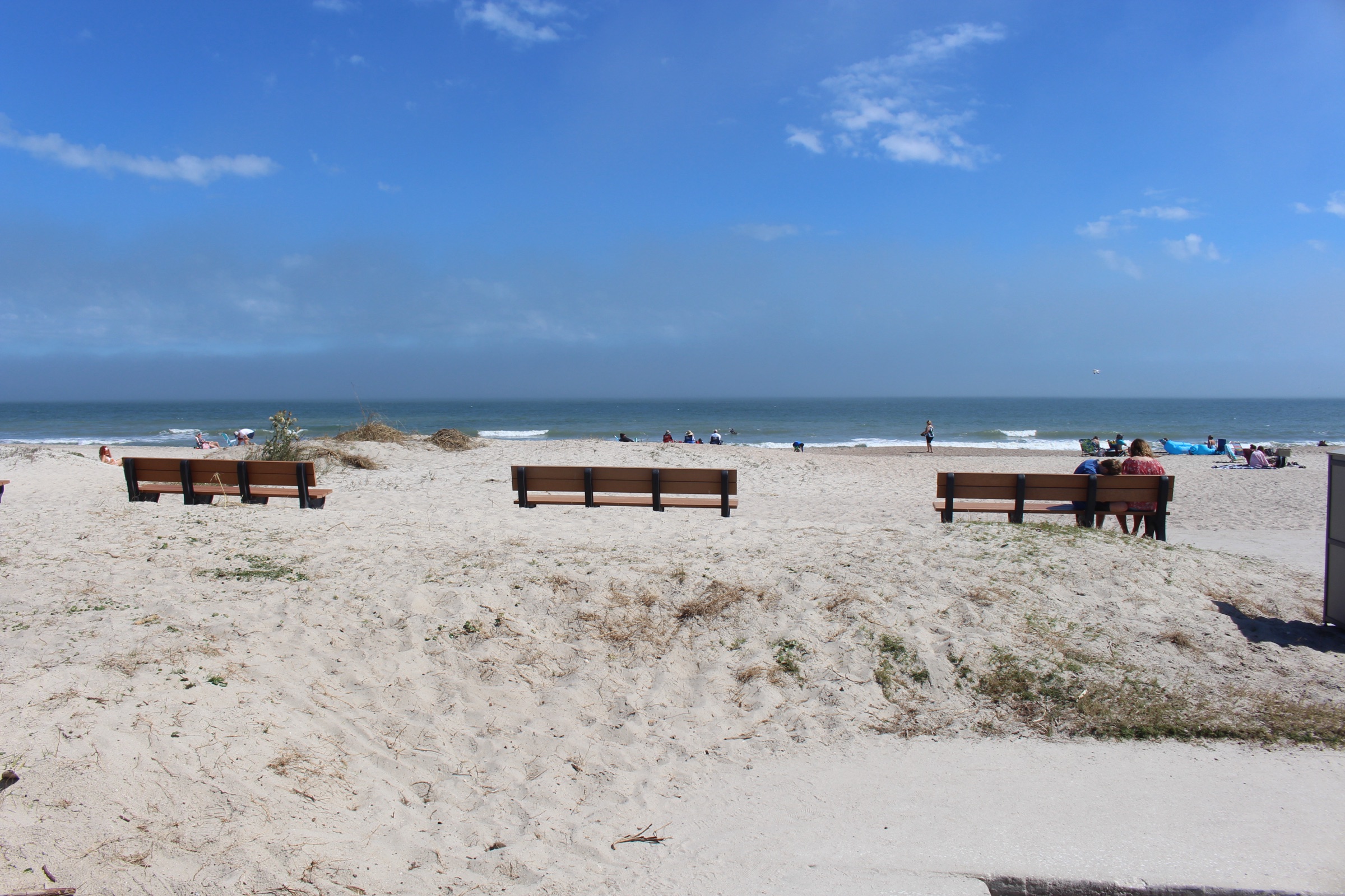 Sandy beach at the Atlantic Avenue public access point in Fernandina Beach, Amelia Island, with a wooden bench in the foreground and the wide Atlantic shoreline stretching into the distance