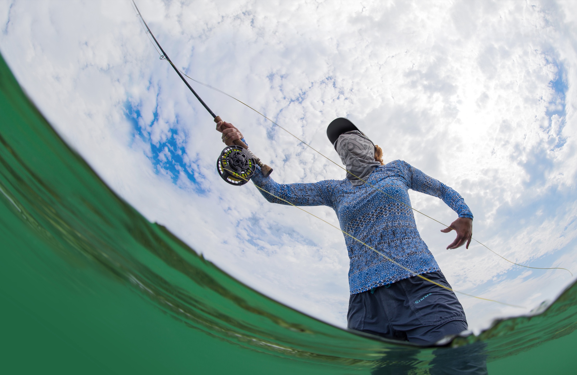 Un pescador vadeando y pescando con mosca en los bajos de sal poco profundos del Santuario Marino Nacional de los Cayos de Florida, rodeado de agua turquesa tranquila e islas de manglar en la distancia.