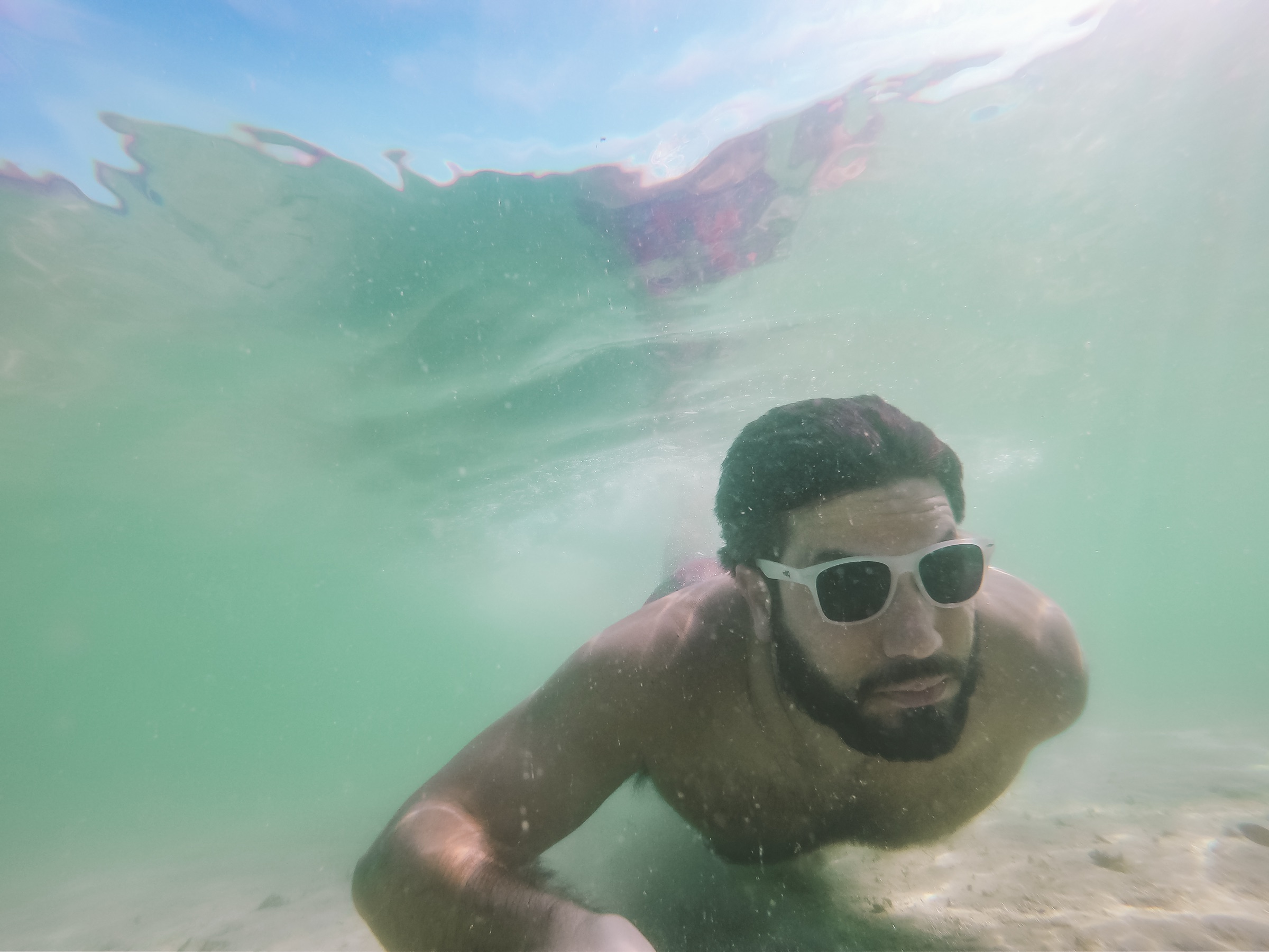Freediver submerged in clear warm water photographed from below, sunlight filtering through the surface