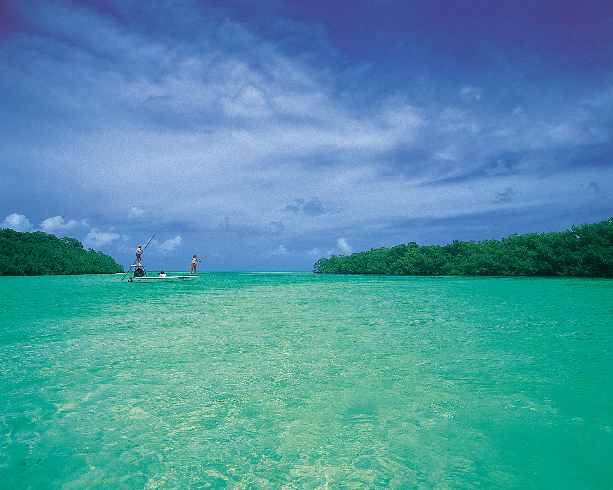 Two anglers flats fishing from a small boat on calm aquamarine water near Islamorada in the Florida Keys, with mangrove islands visible in the background