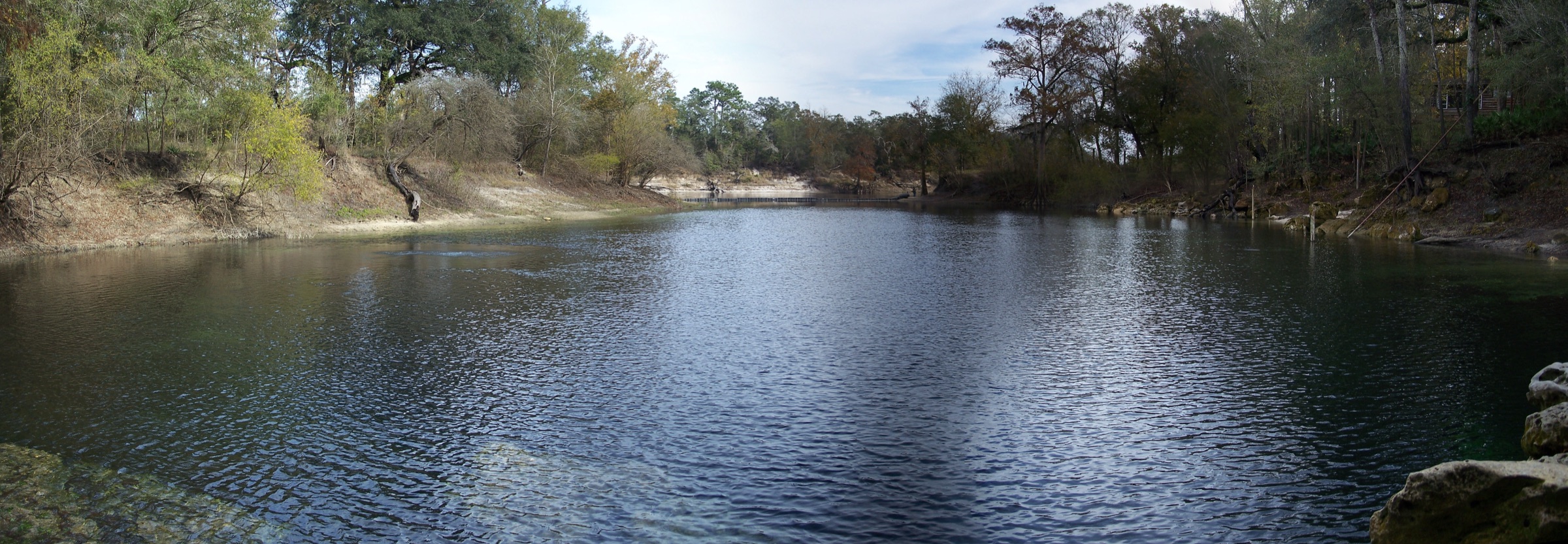 Vista panorâmica da piscina azul-esverdeada e cristalina no Troy Springs State Park, no norte da Flórida, cercada por margens de calcário e vegetação subtropical