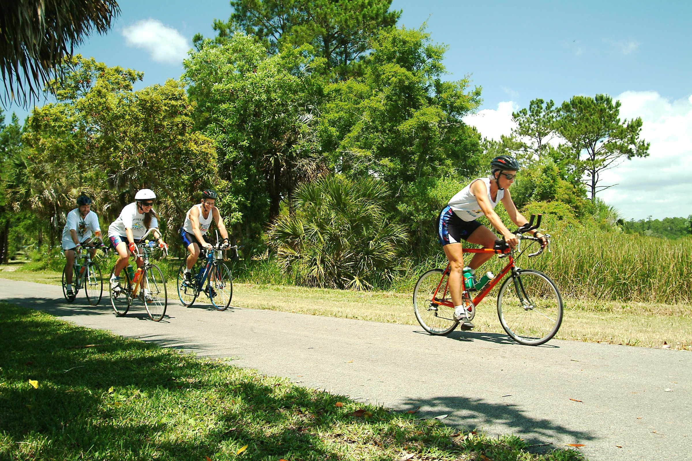 Four cyclists riding side by side through a canopied rail-trail corridor in St. Marks, Florida
